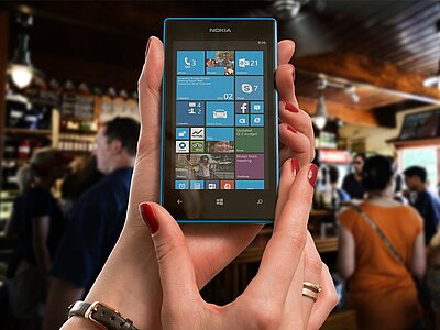 Ein Nokia-Handy, das viele Apps zeigt, im Hintergrund eine Bar, an der mehrere Personen stehen