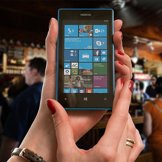 Ein Nokia-Handy, das viele Apps zeigt, im Hintergrund eine Bar, an der mehrere Personen stehen