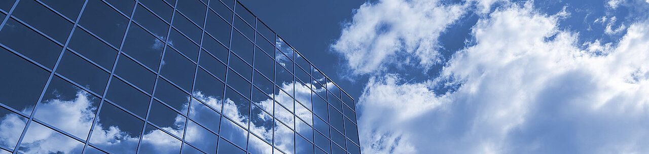 Glasfassade spiegelt blauen Himmel mit weißen Wolken, Himmel rechts sichtbar
