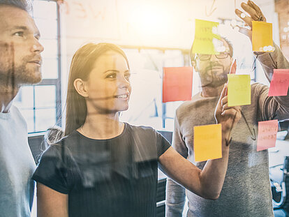 Drei Mitarbeiter schauen sich eine Pinnwand an