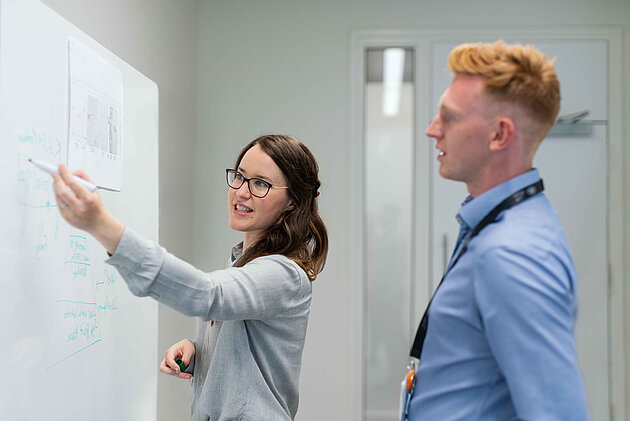 Zwei junge Personen in Businesskleidung besprechen sich vor dem Whiteboard im Büro