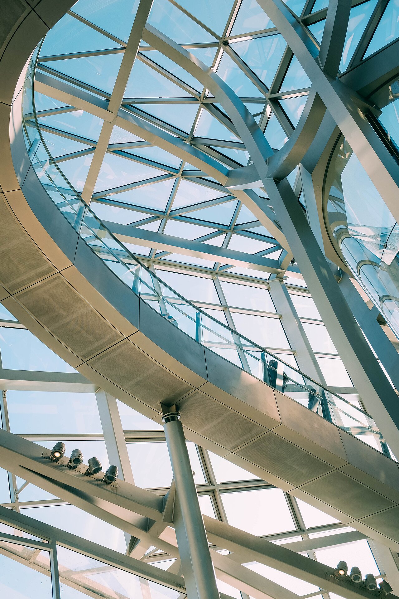 Innenansicht des Gebäudes mit Glasdach und grauen Treppen, im Hintergrund der blaue Himmel