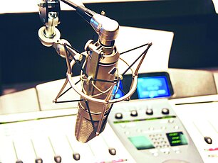 Ein Studiomikrofon in position vor einem Mischpult mit blau leuchtendem Display