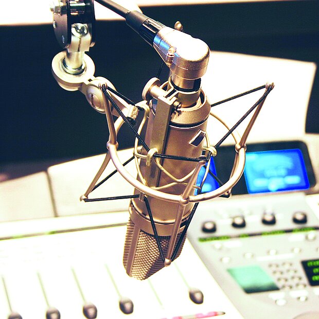 Ein Studiomikrofon in position vor einem Mischpult mit blau leuchtendem Display