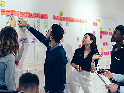 Mehrere Personen besprechen sich vor einer großen Pinnwand