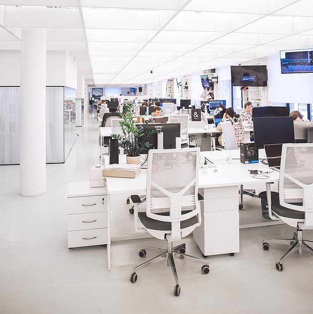 Ein hell erleuchteter, großzügiger Büroraum mit mehreren Personen bei der Arbeit