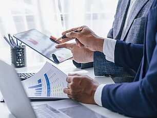 Zwei Personen arbeiten gemeinsam mit Diagrammen und einem iPad am Arbeitsplatz