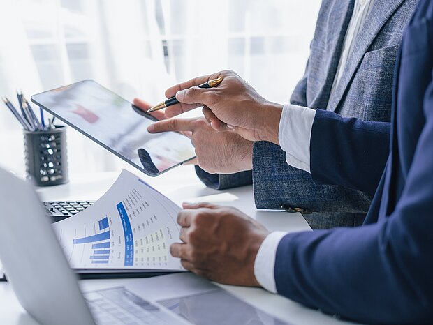 Zwei Personen arbeiten gemeinsam mit Diagrammen und einem iPad am Arbeitsplatz