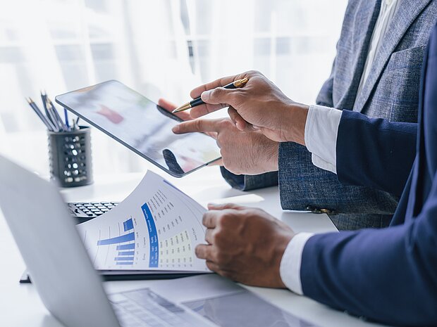 Zwei Personen arbeiten gemeinsam mit Diagrammen und einem iPad am Arbeitsplatz