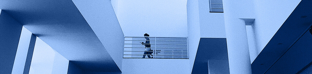 Innenraum eines weiße, futuristischem Gebäude. An einem Geländer läuft eine Person. 