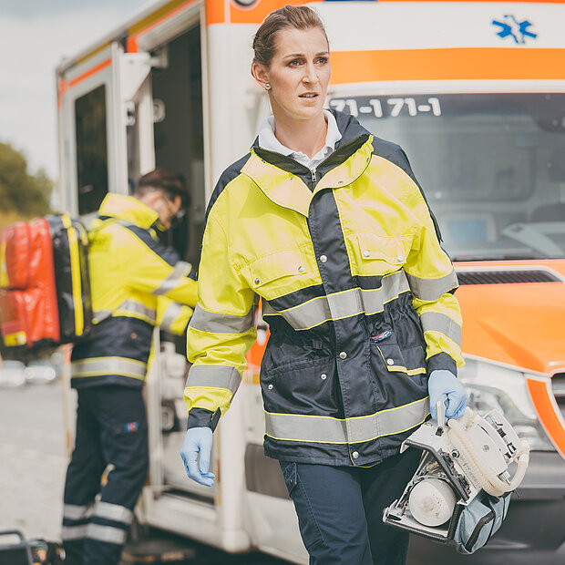 Ein Notarzt holt etwas aus einem Krankenwagen, im Vordergrund eine laufende Notärztin