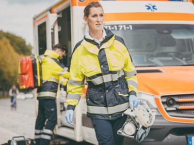 Ein Notarzt holt etwas aus einem Krankenwagen, im Vordergrund eine laufende Notärztin