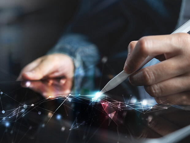 Eine Person die auf einem Tablet mit einem Stift arbeitet. Im Vordergrund Geometrische Formen.