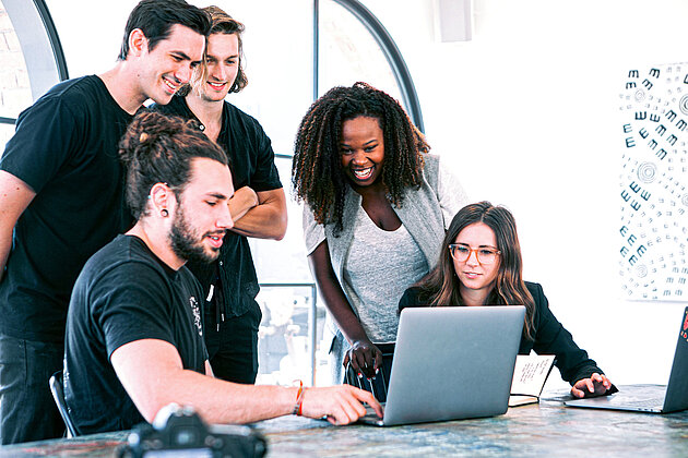 Fünf Personen besprechen etwas auf einem Laptop