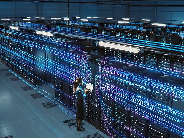 Blick von einer erhöhten position auf einen Serverraum. Zusehen sind mehreren Reihen an blau leuchtenden Server-Schränken.