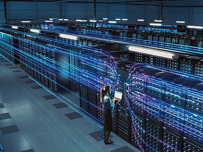 Blick von einer erhöhten position auf einen Serverraum. Zusehen sind mehreren Reihen an blau leuchtenden Server-Schränken.