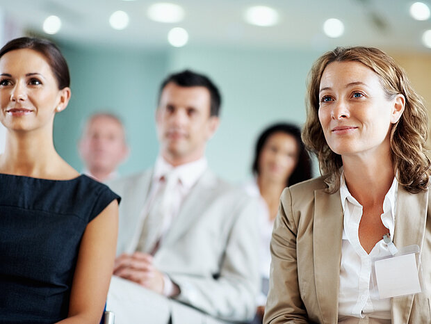 Mehrere Personen schauen in einer Seminarsituation Richtung Kamera.