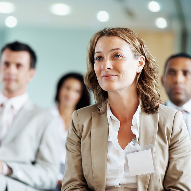 Mehrere Personen schauen in einer Seminarsituation Richtung Kamera.