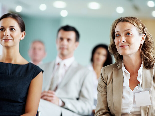 Mehrere Personen schauen in einer Seminarsituation Richtung Kamera.