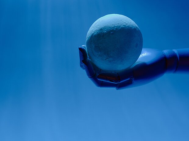 Eine Roboterhand hält eine Kugel vor einem hellblauen Hintergrund.