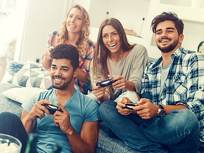 Zwei Männer und zwei Frauen spielen zusammen auf der Couch mit der Konsole