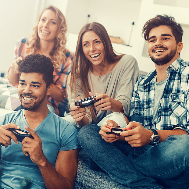 Zwei Männer und zwei Frauen spielen zusammen auf der Couch mit der Konsole