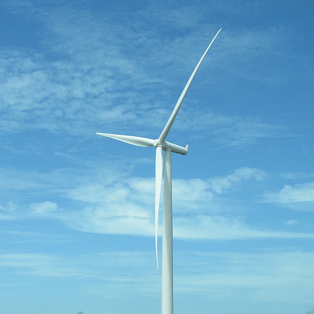 Ein Windrad im Vordergrund des blauen, leicht bewölkten Himmels