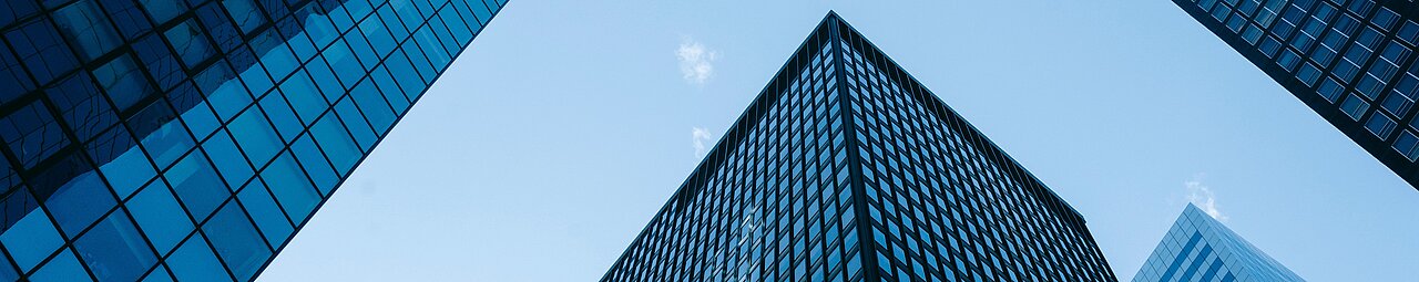 Vier Gebäude spiegeln sich in extremer Perspektive im blauen Himmel.