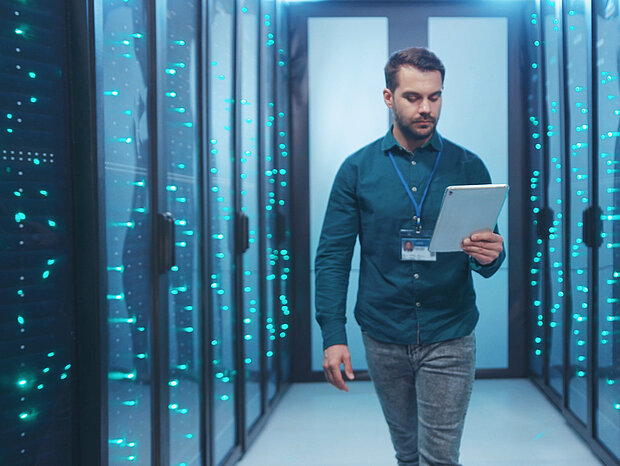 Ein Mann steht mit seinem iPad zwischen den Serverschränken in einem Rechenzentrum