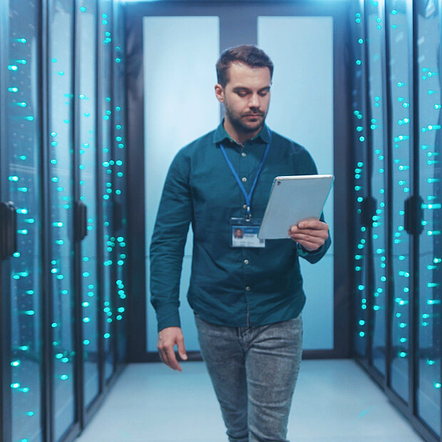 Ein Mann steht mit seinem iPad zwischen den Serverschränken in einem Rechenzentrum