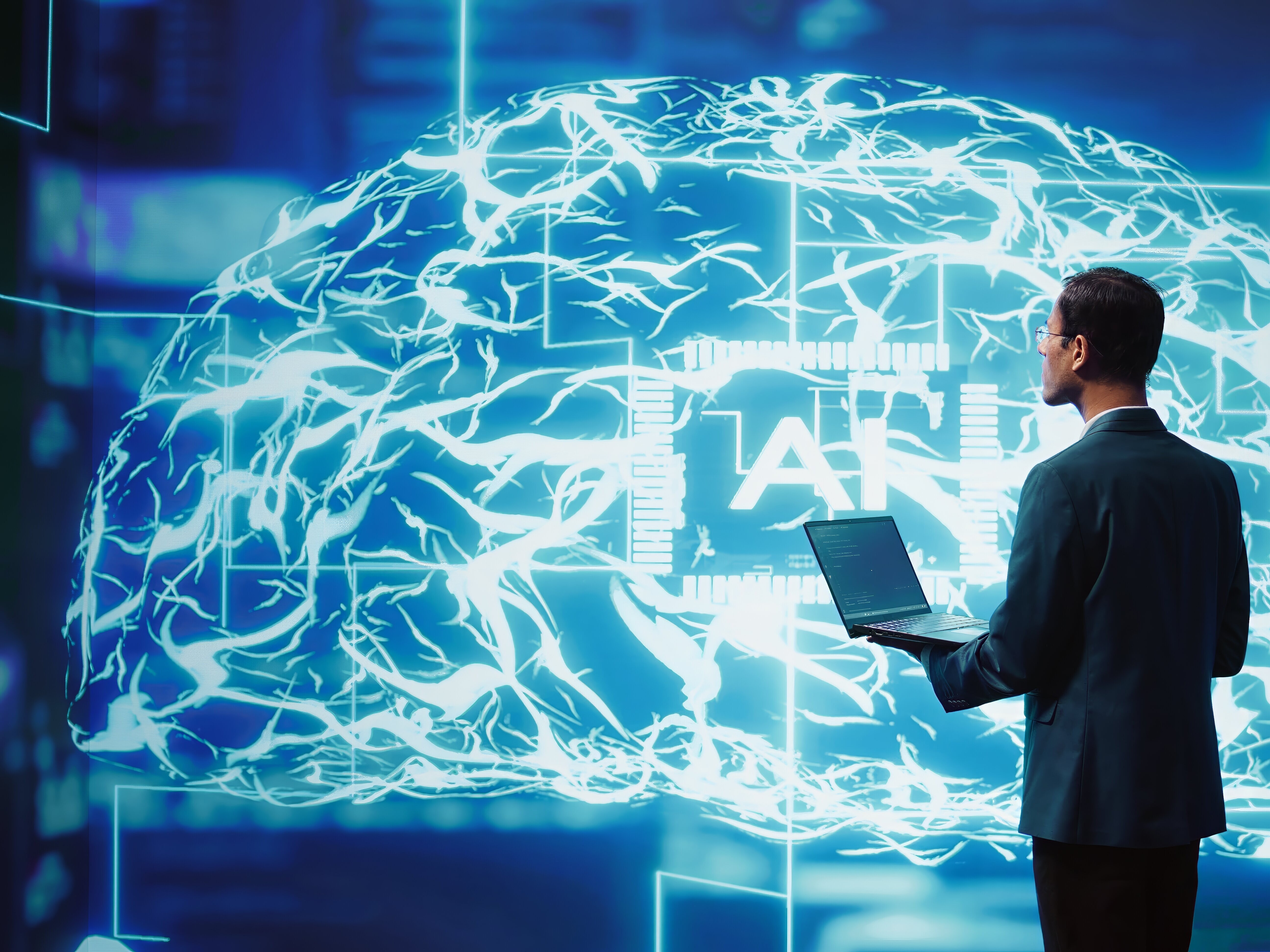 Ein Man mit einem Laptop in der Hand, vor einem digitalem Gehirn. 