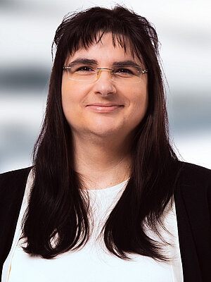 Eine Frau mit braunen Haaren, einer Brille und in schwarz-weißer Kleidung