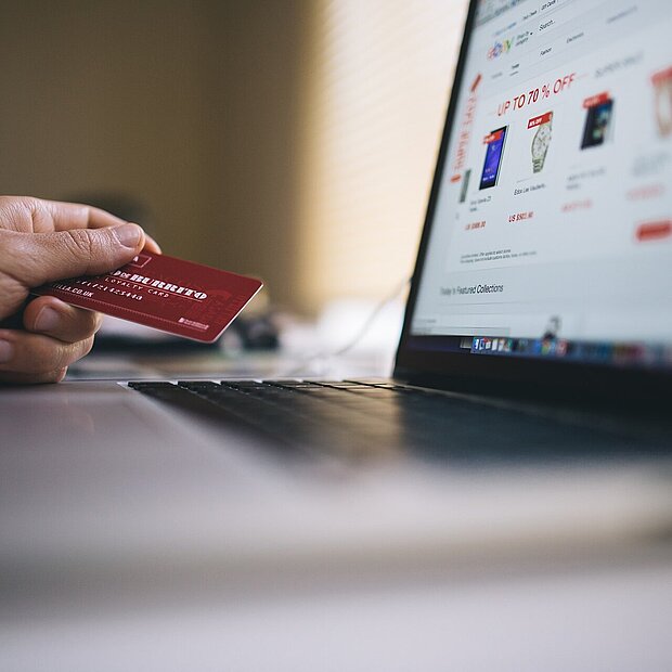 Eine Hand, die eine Kreditkarte hält und auf einen offenen Laptop gelegt ist.