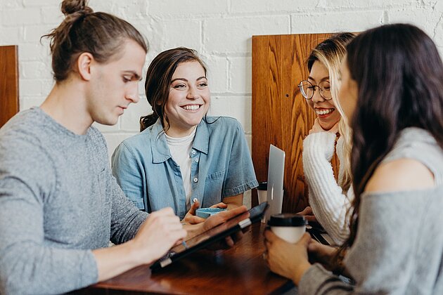 Drei Frauen und ein Mann mit einem iPad sitzen im Café und unterhalten sich