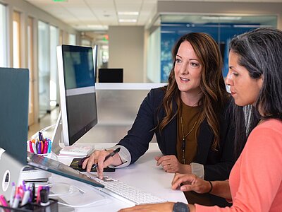 Zwei Sekretärinnen mit einem Laptop und einem Bildschirm am Empfang einer Firma