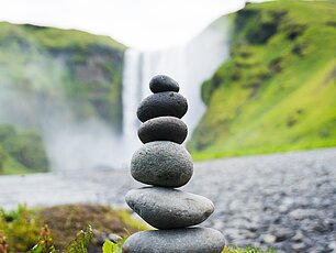 Gestapelte, balancierte Steine im Vordergrund eines Wasserfalls und der Berglandschaft